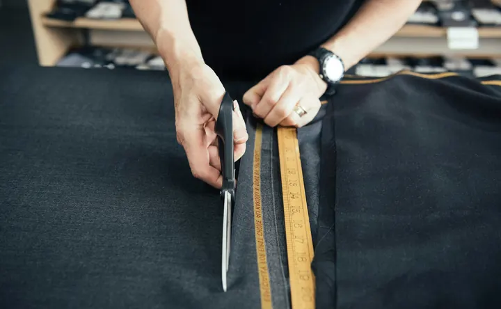 Scissors cutting dark suiting beside two rulers