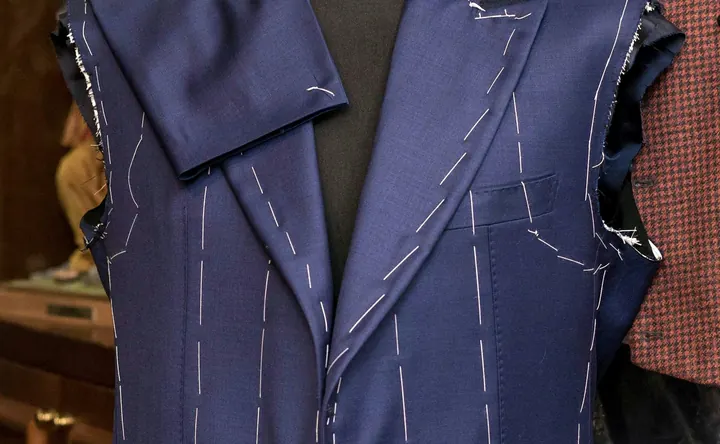 A navy jacket basted in white thread on a dress form